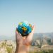 Hand holding a globe against a mountain background symbolizing travel and exploration.