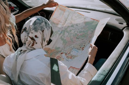 Two friends in a car navigating their road trip using a map during daytime.