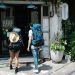 Back view of anonymous couple of tourists with rucksacks walking on street and entering hostel door during trip